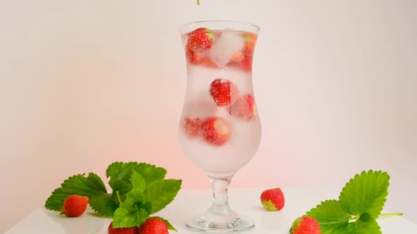 Bebidas de verano. Bebida de fresa. agua con hielo y fresas en un vaso de vidrio y fresas maduras con hojas. Una mano pone menta en un vaso de cóctel. Refrescante cóctel de verano. — Vídeos de Stock