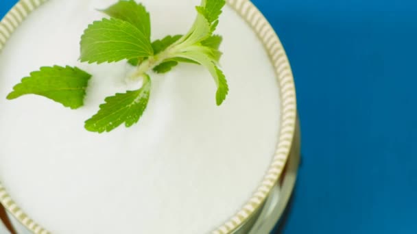 Stevia en un tazón verde con polvo blanco de stevia sobre fondo azul de madera.Rotación.Stevia rebaudiana. Vista desde arriba.Edulcorante natural orgánico.Plantas de stevia. — Vídeo de stock