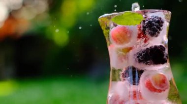 Böğürtlen ve böğürtlen kokteyli, nane ve buz küpleri güneş altında bir yaz bahçesinde. Buzlu böğürtlen içeceği. 