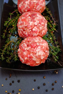 Çiğ kıymalı domuz eti. Köfteler yakın plan. Kıymalı köfteler, siyah bir arkaplanda siyah bir plaka üzerinde kekik ile dizilmiş. Et üretimi. Çiftlik eti..