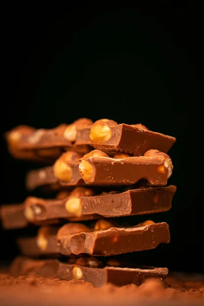 Kaputte Schokolade. Schokoladenstücke mit Nüssen stapeln sich auf schwarzem Hintergrund. Schokolade mit Haselnüssen und Kakaopulver. Desserts und Süßigkeiten. Vollmilchschokolade mit Nüssen — Stockfoto