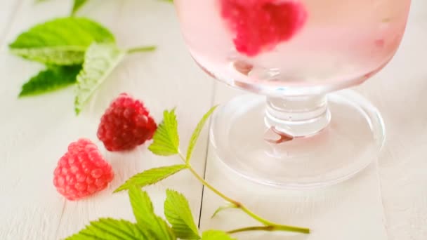 Малина коктейль. Літній напій. Кубики льоду з малиною в склянці з мінеральною водою, ягодами та листя малини на білому дерев'яному столі . — стокове відео