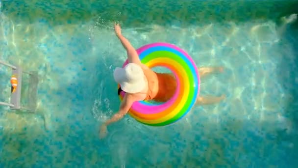 Child swims in the swimming pool.Girl in a hat with a rainbow inflatable ring in the pool. View from above.Summer time and holidays. Summer weather.slow motion. — Stock Video