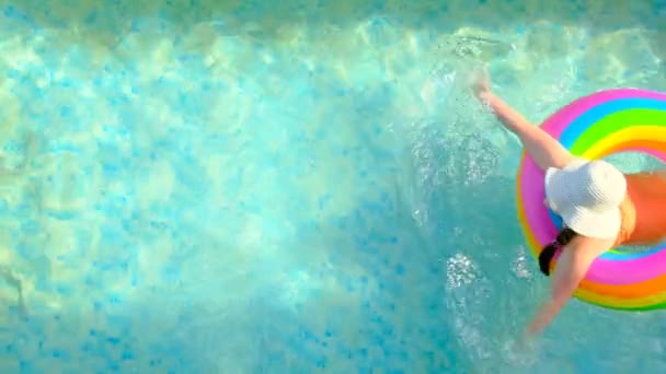 Sommartid.Barn simmar i poolen.Flicka i hatt med en regnbåge uppblåsbar ring i poolen. Utsikt uppifrån. Sommarväder. slow motion.. — Stockvideo