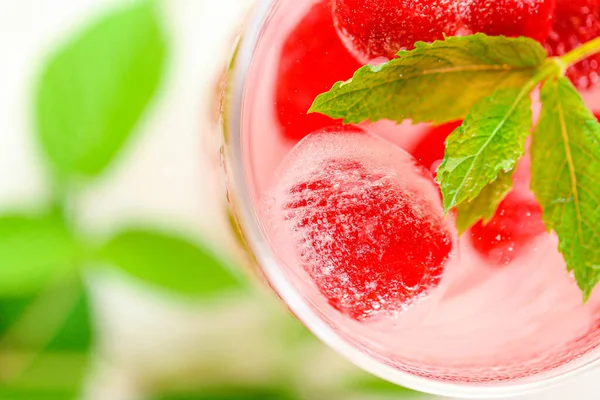 Bevanda estiva.Bevanda rosa lampone.Cubetti di ghiaccio con lamponi in un bicchiere con acqua, bacche e foglie di lampone su un tavolo di legno bianco. cocktail rinfrescante. Cocktail al lampone. — Foto Stock