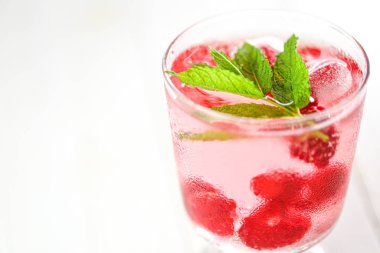 Ahududulu kokteyl. Ahudududulu pembe içecek. Ahudududulu buz küpleri. Su, böğürtlen ve ahududu yapraklı beyaz bir masa. ferahlatıcı kokteyl.