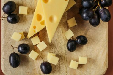 Mazdar peyniri üçgenleri, gouda peyniri küpleri ve siyah üzümler. Ahşap arka planda üzümlü peynir. Süt yağı ve süt ürünleri..