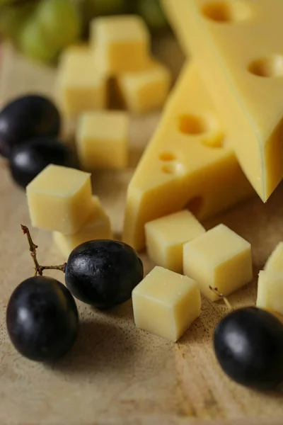 Mazdar cheese triangles, gouda cheese cubes and black and green grapes.Cheese with grapes berries on wooden background.