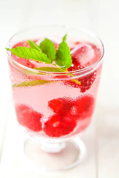 Cocktail.Summer lampone drink.Raspberry rosa drink.Ice cubetti con lamponi in un bicchiere con acqua, bacche e foglie di lampone su un tavolo di legno bianco — Foto Stock