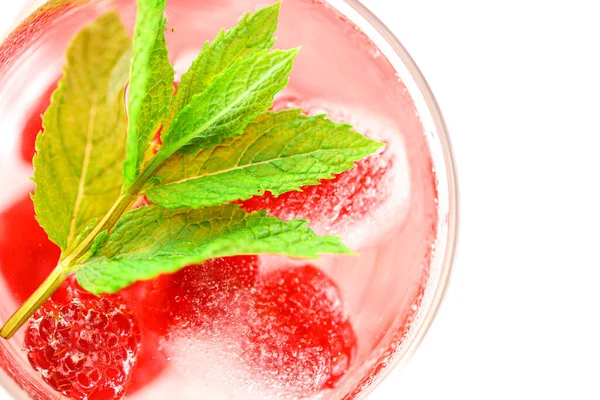 Cóctel refrescante. Coctel de frambuesa.Bebida de verano.Bebida rosa de frambuesa.Cubos de hielo con frambuesas en un vaso con agua, bayas y hojas de frambuesa en una mesa de madera blanca. —  Fotos de Stock