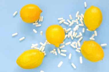 Mavi arka planda C vitamini beyaz haplar ve sarı limonlar. Doğal meyve vitamini C. Sağlık ve ilaç. Vitaminler ve mineraller..