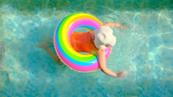 Flicka i hatt med en regnbåge uppblåsbar ring i poolen. — Stockvideo