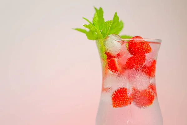 Bevanda alla fragola.Bevande estive.Cocktail rinfrescante. acqua in vetro con ghiaccio e fragole. Acqua minerale con ghiaccio e fragole in un calice di vetro e fragole mature con foglie. — Foto Stock