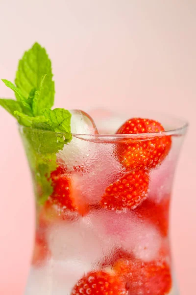 夏の飲み物。さわやかなカクテル。氷とイチゴの入ったガラスの水。氷とイチゴをガラスのゴブレットに入れたミネラルウォーターと葉を持つ熟したイチゴ. — ストック写真