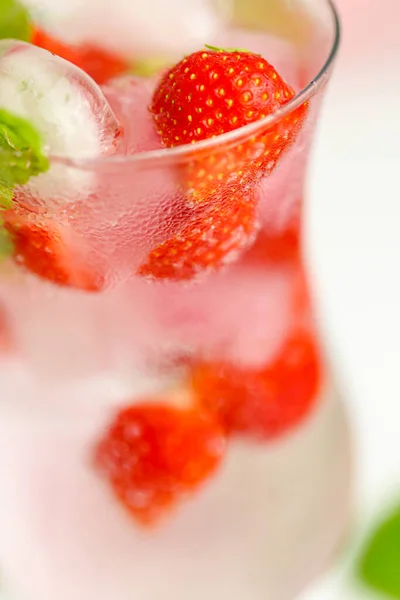 ストロベリードリンク夏のドリンク。氷とイチゴと一緒に水を。氷とイチゴをガラスのゴブレットに入れたミネラルウォーターと葉を持つ熟したイチゴ. — ストック写真