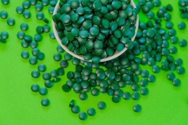 Yuvarlak bir kaseye, yeşil spirulina hapları. Yeşil fonda. Vitaminler ve besin takviyeleri