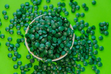 Alevli su yosunu tabletleri. Bir kasenin içine haplar. Yeşil arka planda spirulina tabletleri. Vitaminler ve besin takviyeleri