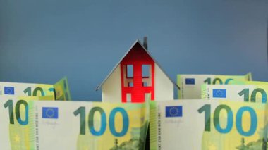Emlak piyasası. Emlak fiyatları. İpotekler ve konut giderleri. Ev almak ve inşa etmek. Gri çatılı ve 100 Euro 'luk banknotları olan sahte ev. Emlak borcu. Ev ve para.