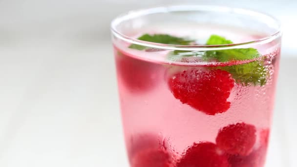 Raspberry cocktail.Splashes and drops of a Summer drink. glass with raspberry drink.raspberries in a glass with water, berries and raspberry leaves on a white wooden table. — Stockvideo