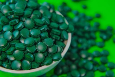 Yuvarlak bir kaseye koyulan bir ilaç. Yeşil spirulina tabletleri yeşil arka planda. Brüksel yosun tabletleri. Vitaminler ve beslenme takviyeleri. Daha besleyici yiyecekler. Sağlıklı bir yaşam tarzı için gıda takviyeleri.