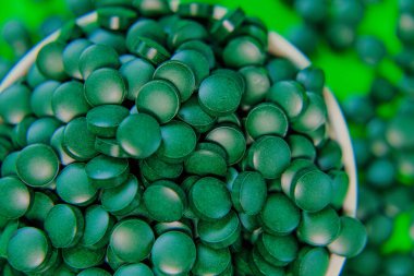 Yuvarlak bir kaseye koyulan bir ilaç. Yeşil spirulina tabletleri yeşil arka planda. Brüksel yosun tabletleri. Süper yemek. Sağlıklı bir yaşam için gıda takviyesi.