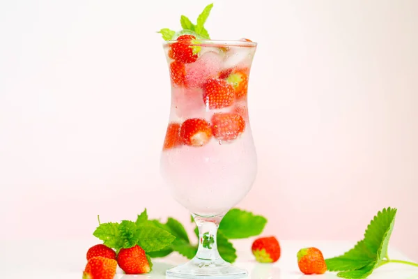 Bevi fragole. Cocktail estivo.Bicchiere d'acqua minerale con ghiaccio e fragole mature con foglie su sfondo rosa chiaro. Bevanda dalle bacche estive — Foto Stock
