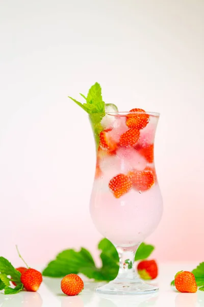 Bevi fragole. Cocktail.Summer estate drink.mineral bicchiere d'acqua con ghiaccio e fragole mature con foglie su sfondo rosa chiaro. — Foto Stock