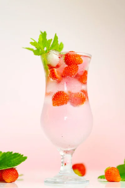 Клубничный напиток. летний коктейль. Стакан минеральной воды со льдом и спелая клубника с листьями на светло-розовом фоне. — стоковое фото