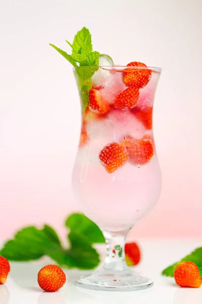Bevi fragole. Cocktail estivo.Bicchiere d'acqua minerale estivo con ghiaccio e fragole mature con foglie su sfondo rosa chiaro. — Foto Stock