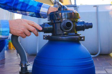 Havuz filtresi. Su filtresi. Su filtresi bir adamın elinde. Yüzme havuzu temizleme ekipmanı. Bir adam hortumları havuzun filtresine taşıyor..