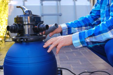 Su filtresi. Su filtresi havuz kenarındaki bir adamın ellerinde. Yüzme havuzu temizleme ekipmanı. Bir adam hortumları havuzun filtresine taşıyor..