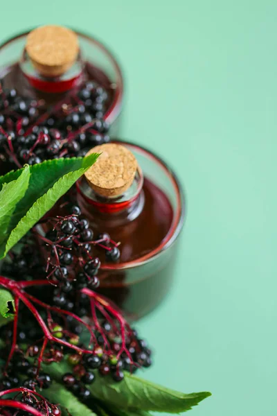 Elderberry syrup.Red elderberry 시럽을 유리병에 넣고 초록 배경에 잘 익은 검은 엘 더 베리를 넣는다. 대체 의학 과 동종 요법 . 엘더 베리 수확 — 스톡 사진