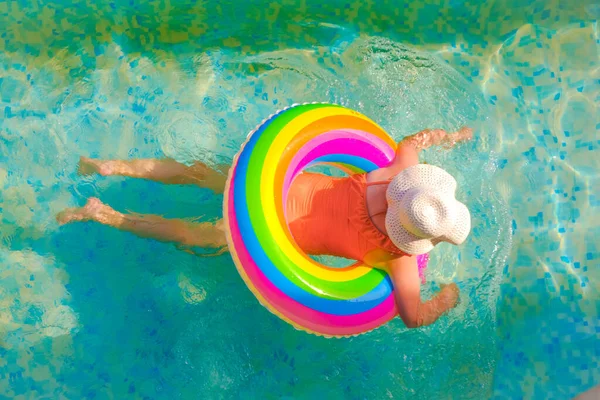 El niño nada en la piscina.Temporada de baño.Tiempo de verano y vacaciones. Chica con un anillo inflable arco iris en la piscina en un día soleado de verano —  Fotos de Stock