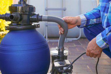  Havuz filtresi. Evin yakınındaki terasta yüzme havuzu temizleme ekipmanı. Adam hortumları havuzun filtresine taşıyor..