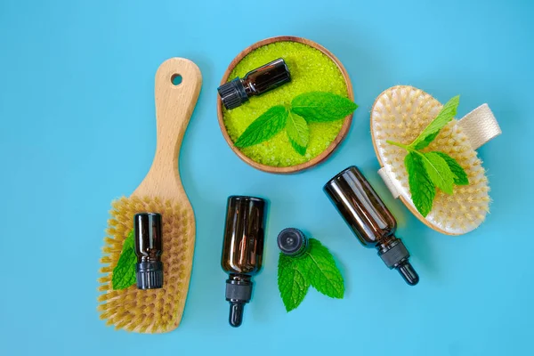 Peppermint salt.bristle body brushes, green sea salt in wooden bowl and sprigs of peppermint on blue background. Natural cosmetics and aromatherapy.Organic natural cosmetics for body with mint extract