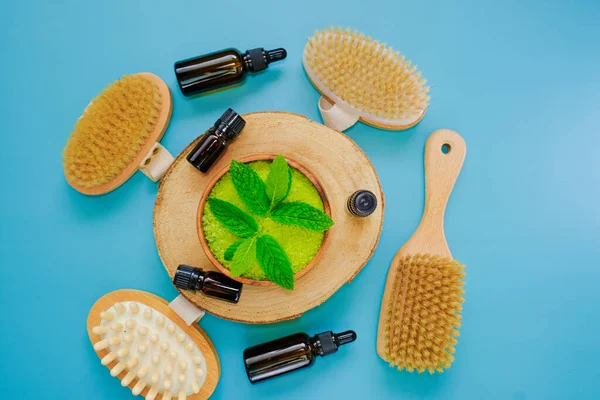 cosmetics for body with mint extract. Peppermint salt.bristle body brushes, green sea salt in a wooden bowl and sprigs of peppermint on a bright blue background. Natural cosmetics and aromatherapy.