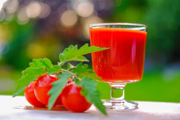 Tomato juice in a glass goblet and ripe red tomatoes on a green summer garden background.Vegetable juices. Red tomato organic juice