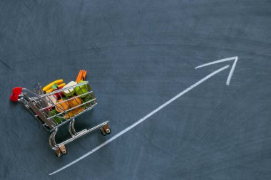 Rising food prices.food crisis.Rise in the price of the grocery basket. supermarket trolley with groceries and up arrow on black chalk board background. Food prices.