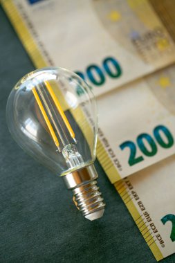 Elektrik faturası. Ampul, avro banknotları ve tebeşir tahtasındaki madeni paralar. AB ülkelerindeki enerji üretim krizinin maliyetinin artırılması..