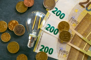 Avrupa 'da artan elektrik fiyatları. Elektrik kavramından tasarruf. Elektrik maliyeti. Ampul, euro banknotları ve kara tebeşir tahtasında bulunan madeni paralar. Işık ve ısının maliyetini artırıyor..