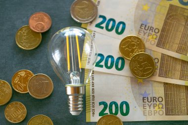 Elektrik faturası. Ampul, avro banknotları ve kara tebeşir tahtasındaki madeni paralar. Avrupa 'da elektrik fiyatlarının yükseltilmesi. AB ülkelerinde enerji üretimi krizi.