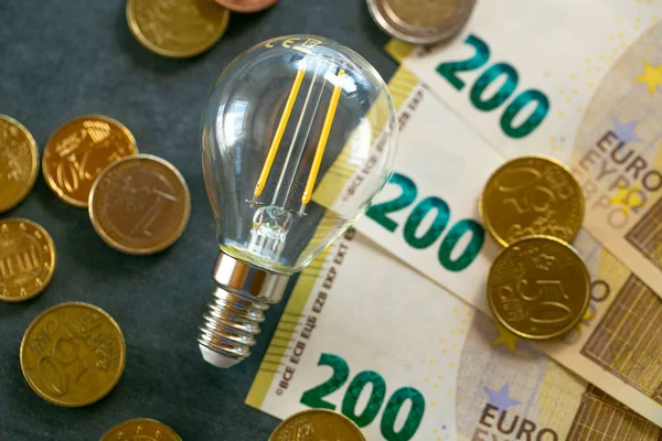 Rising electricity prices in Europe.Light bulb,banknotes and coins on chalk board.Increasing the cost of light and heat.Saving electricity concept.Crisis of energy production in the EU countries.