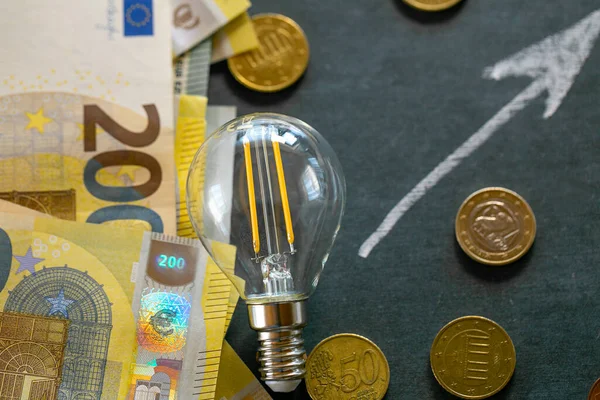 Rising electricity prices in Europe. Light bulb,euro bills and euro coins.Crisis of energy production in the EU countries.Increasing the cost of light and heat.Saving electricity concept