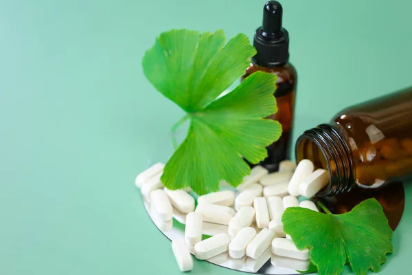 ginkgo biloba leaf and white tablets with ginkgo biloba extract on green background.Preparations with ginkgo biloba extract.Alternative medicine and homeopathy.Green natural pharmacy.