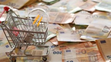Electricity cost. Electricity bills.Rising electricity prices in Europe. Light bulb in a shopping cart,euro bills.Hands count euro bills on euro banknotes background.Crisis of energy production 