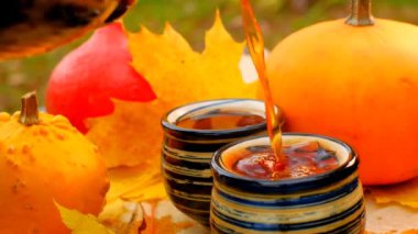Tea drinking in the garden on a sunny day.Hot tea is poured in mugs. Autumn tea. mugs with hot drink and pumpkins with maple leaves in a cold autumn garden.Cozy tea party in the autumn garden. Autumn