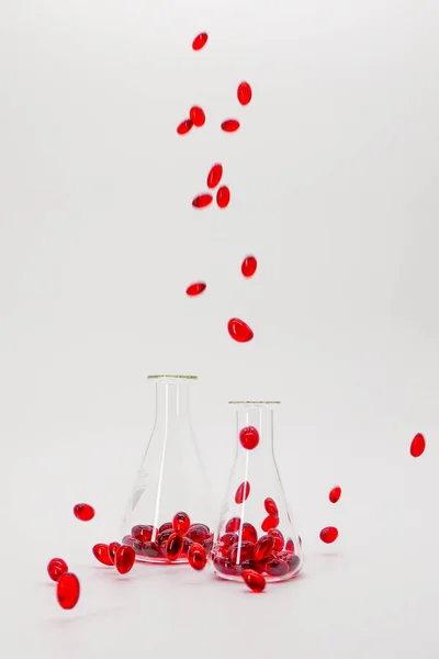 Krill oil red gelatin capsules in laboratory transparent flasks on a white background.natural omega three acids.Source of omega 3 fatty acids.Natural supplements and vitamin