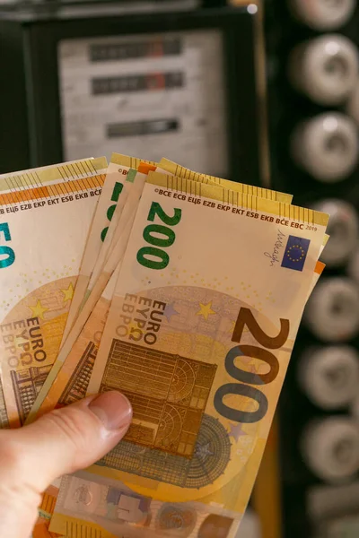 Paying electricity bills in Europe. Hand holding euro bills on electric meter background. Rising electricity prices.Payment for utility services