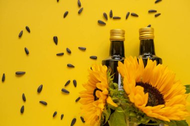  Oil bottles, scattered black sunflower seeds and sunflowers blooming on a bright yellow background. Organic natural farm sunflower oil. Edible oils.top view
