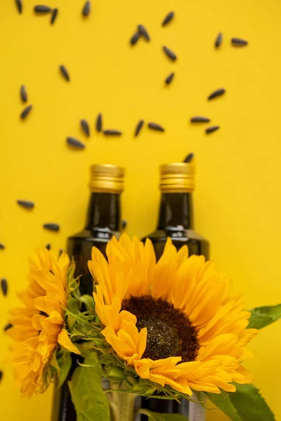 Sunflower oil. Oil bottles, scattered black sunflower seeds and sunflowers blooming on a bright yellow background. Organic natural farm sunflower oil. Edible oils.top view